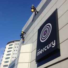 A team of workers suspended in harnesses, using rope access methods to access and work on a building's exterior.
