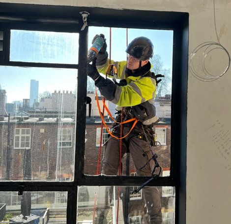 A worker using rope access methods to reach challenging areas of a building, ensuring thorough inspection and maintenance.