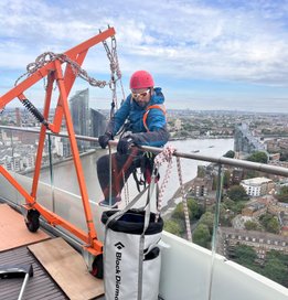 A worker suspended in mid-air using rope access equipment to conduct maintenance work on the exterior of a tall building